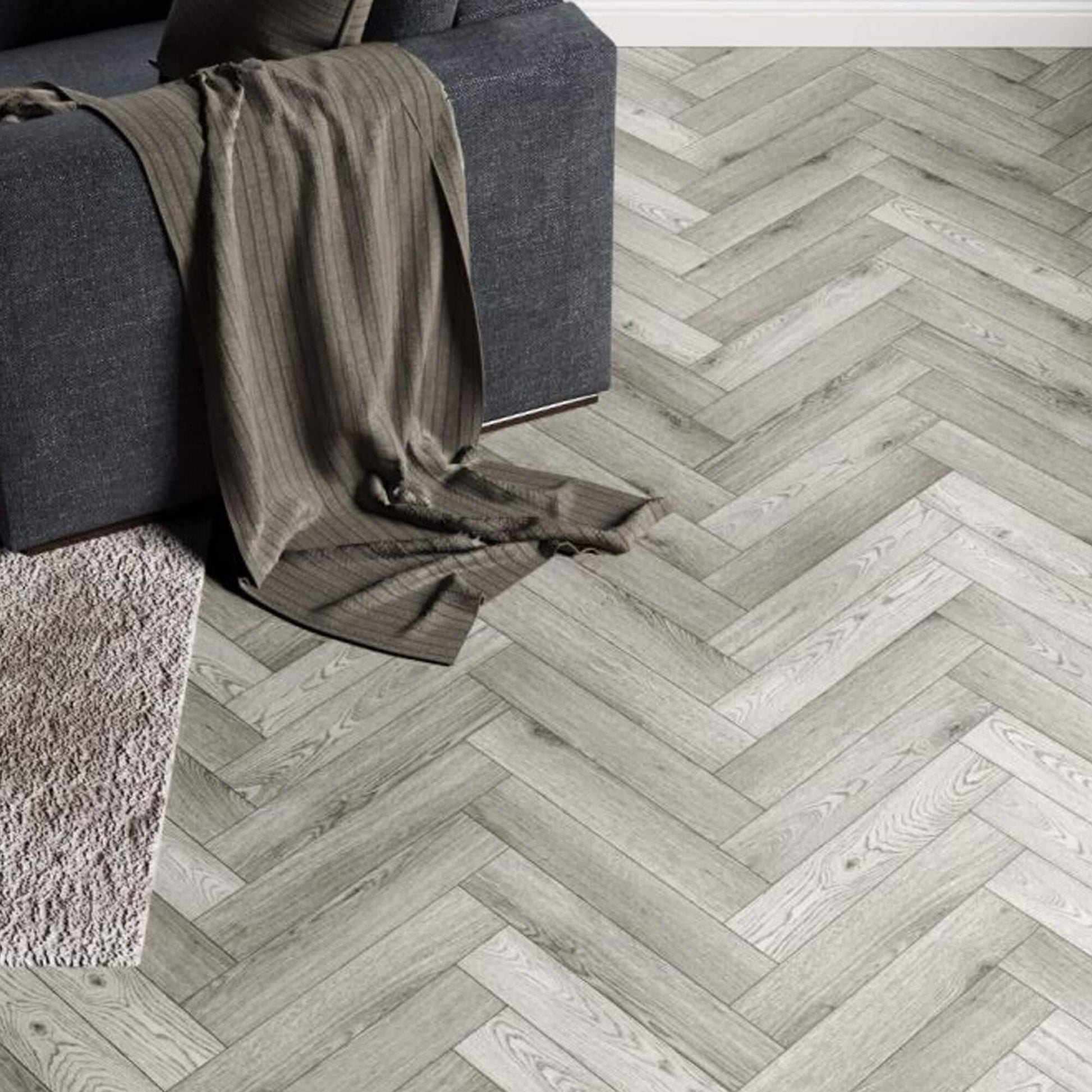 Alsace Oak Rigid LVT Herringbone Flooring with a sofa in the corner.
