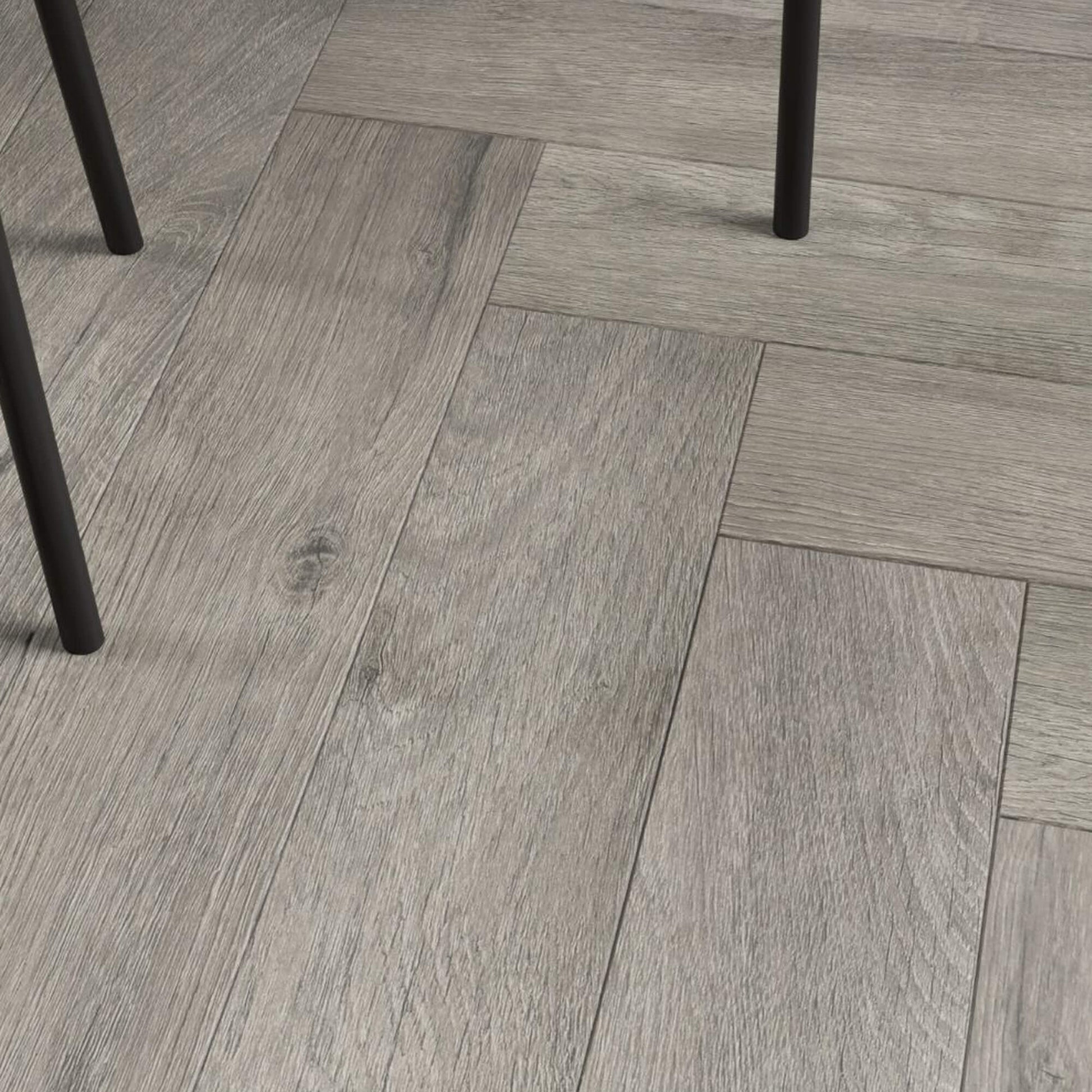 Close-up of Castle Grey Herringbone Laminate Flooringn and black chair  legs visible.