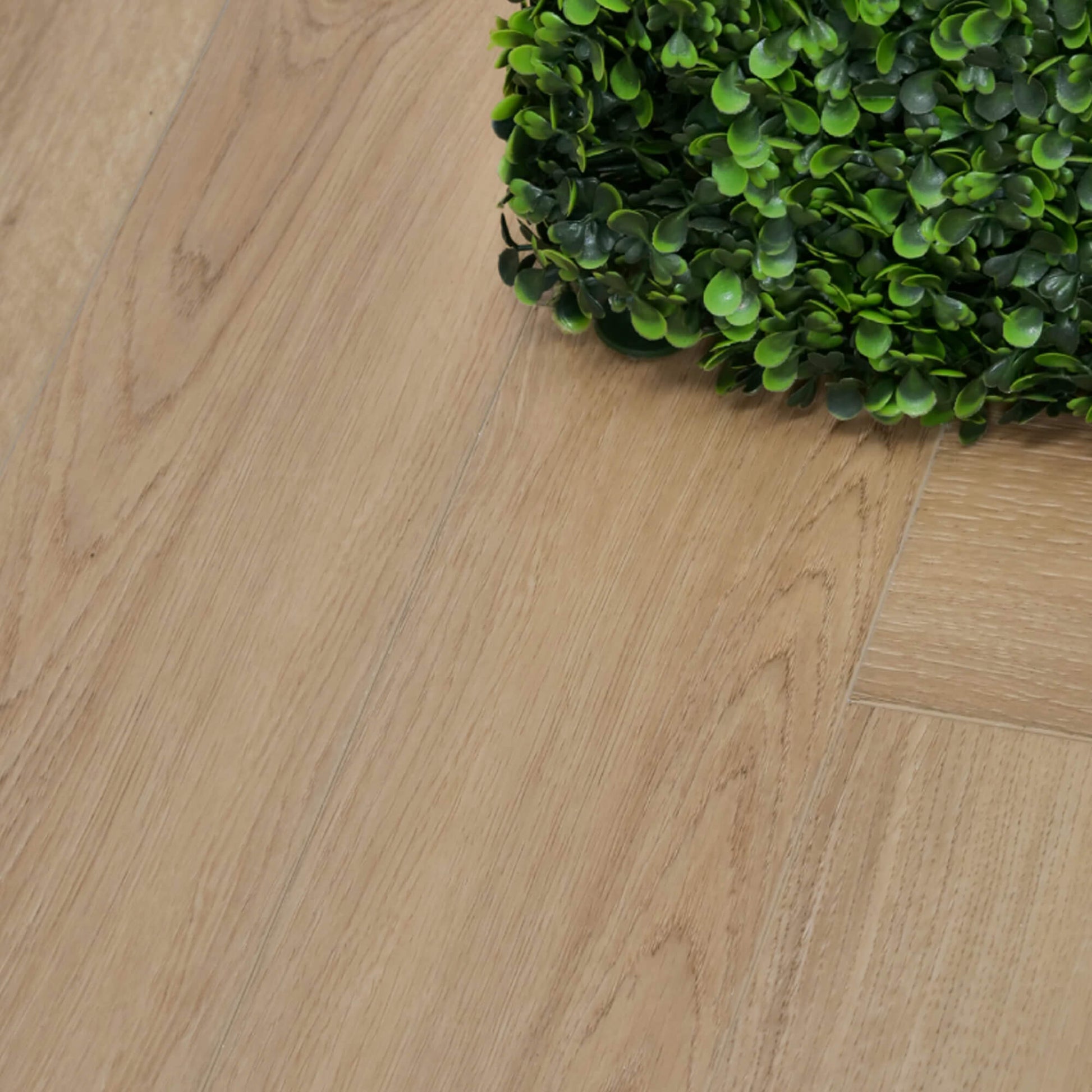 Close-up of Heritage Oak Rigid LVT Herringbone Flooring with a green plant in the corner.