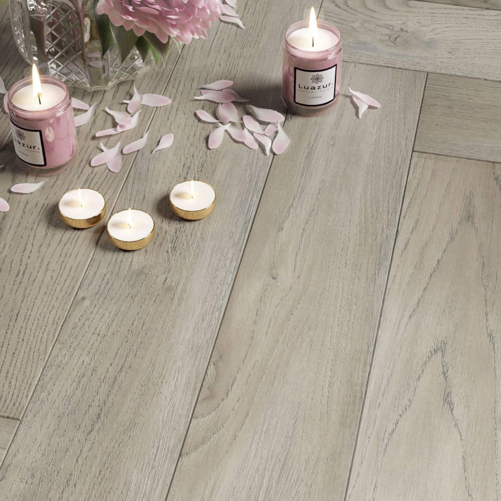 Close-up of Manor Grey Oak Herringbone Laminate Flooring with candles in the background.