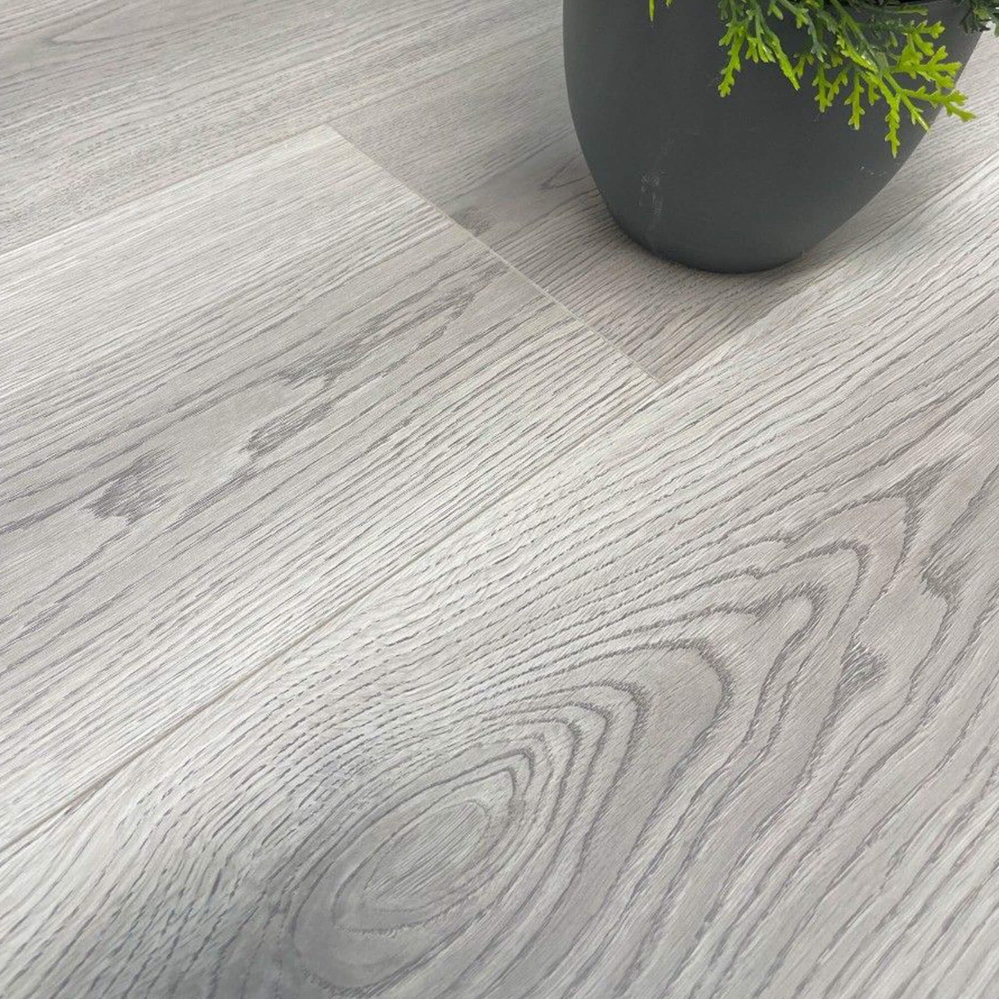 Close-up of Misty Grey Prestige Plus Laminate Flooring with a flower pot in the background.