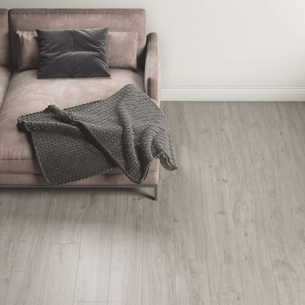 Rockford Oak Laminate Flooring in a living room interior setting with a sofa, pillows and a rug in the background.