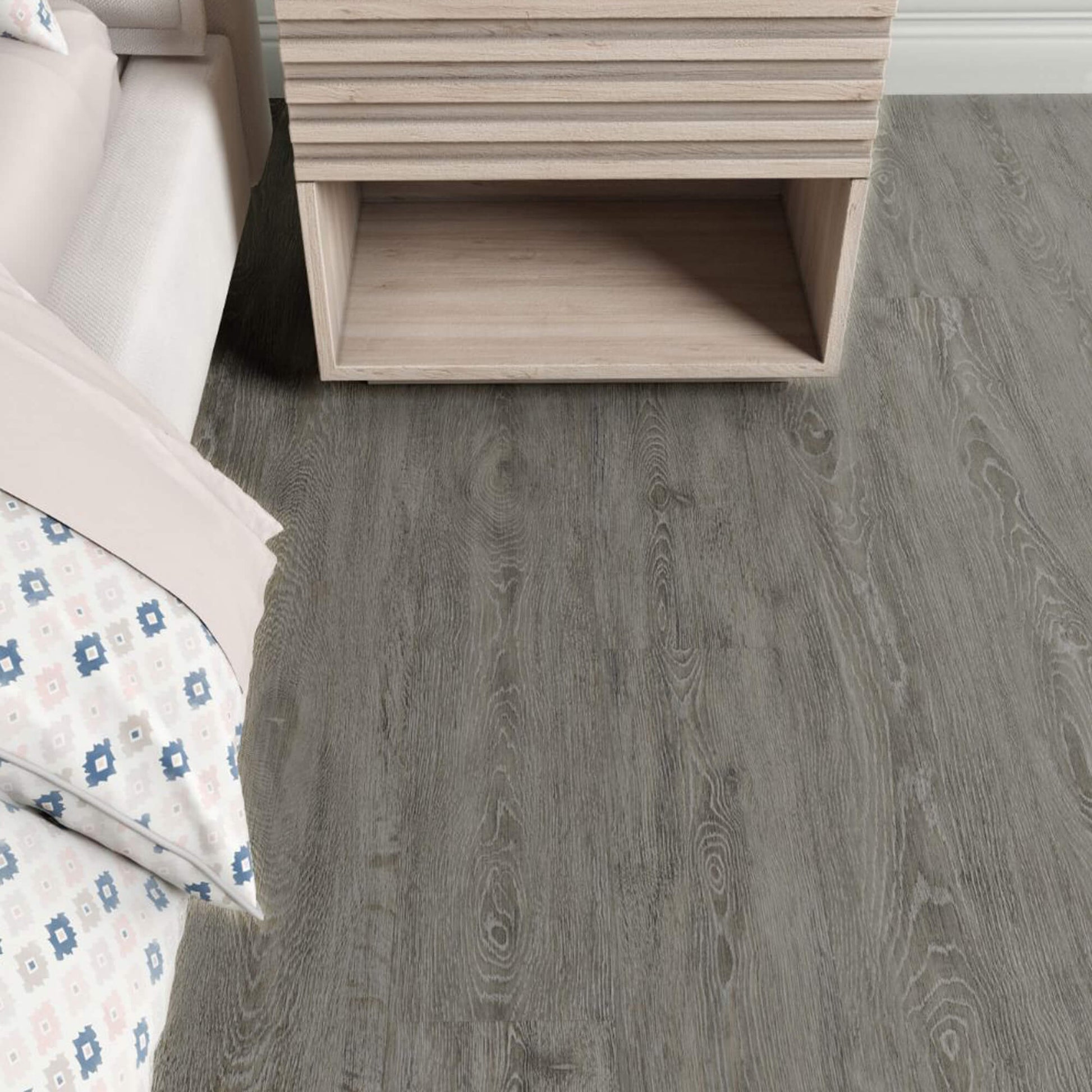 Wooden nightstand next to a bed with floral bedding on Weathered Oak Rigid LVT flooring.